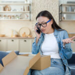 Unsatisfied woman received a broken parcel delivered from an online online store, Asian quarrels with the customer support service, talks to the operator on the phone, sitting home in the kitchen.